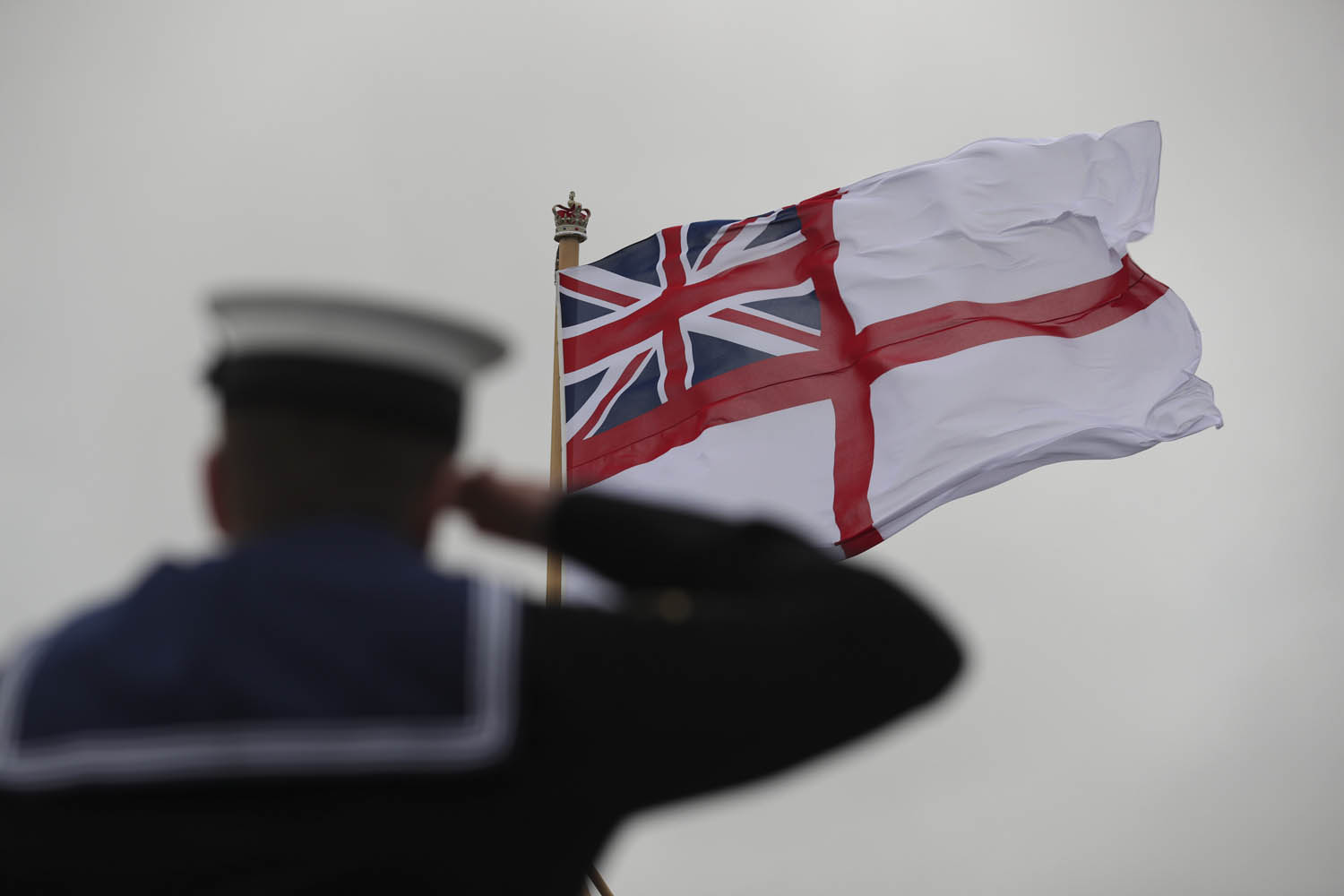 The White Ensign being hosted as a sailor salutes onboard HMS Prince of Wales for the first time during her commissioning