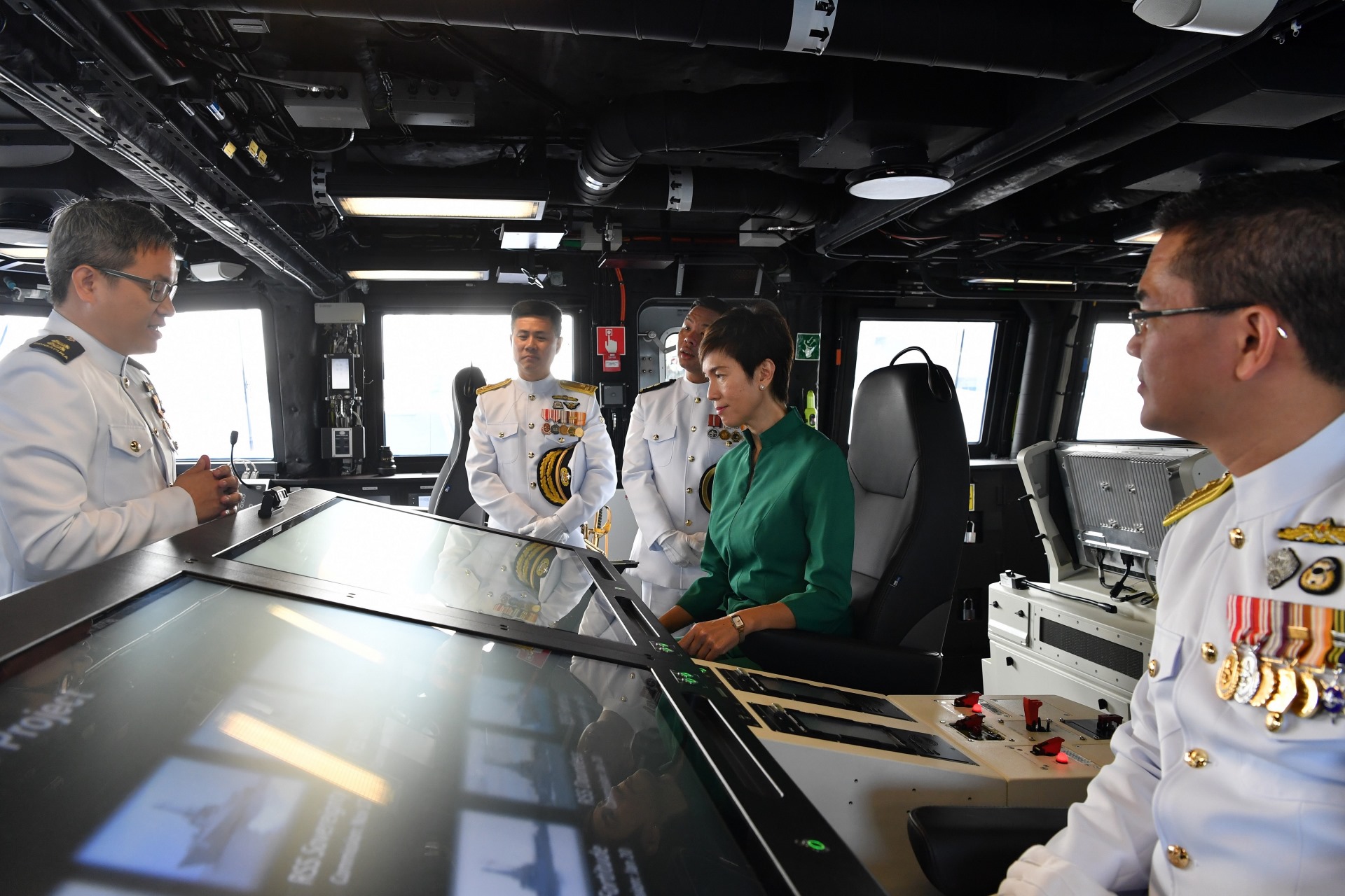 Minister Josephine Teo receiving a brief at RSS Dauntless' Integrated Command Centre, accompanied by the Chief of Navy Rear-Admiral Lew Chuen Hong