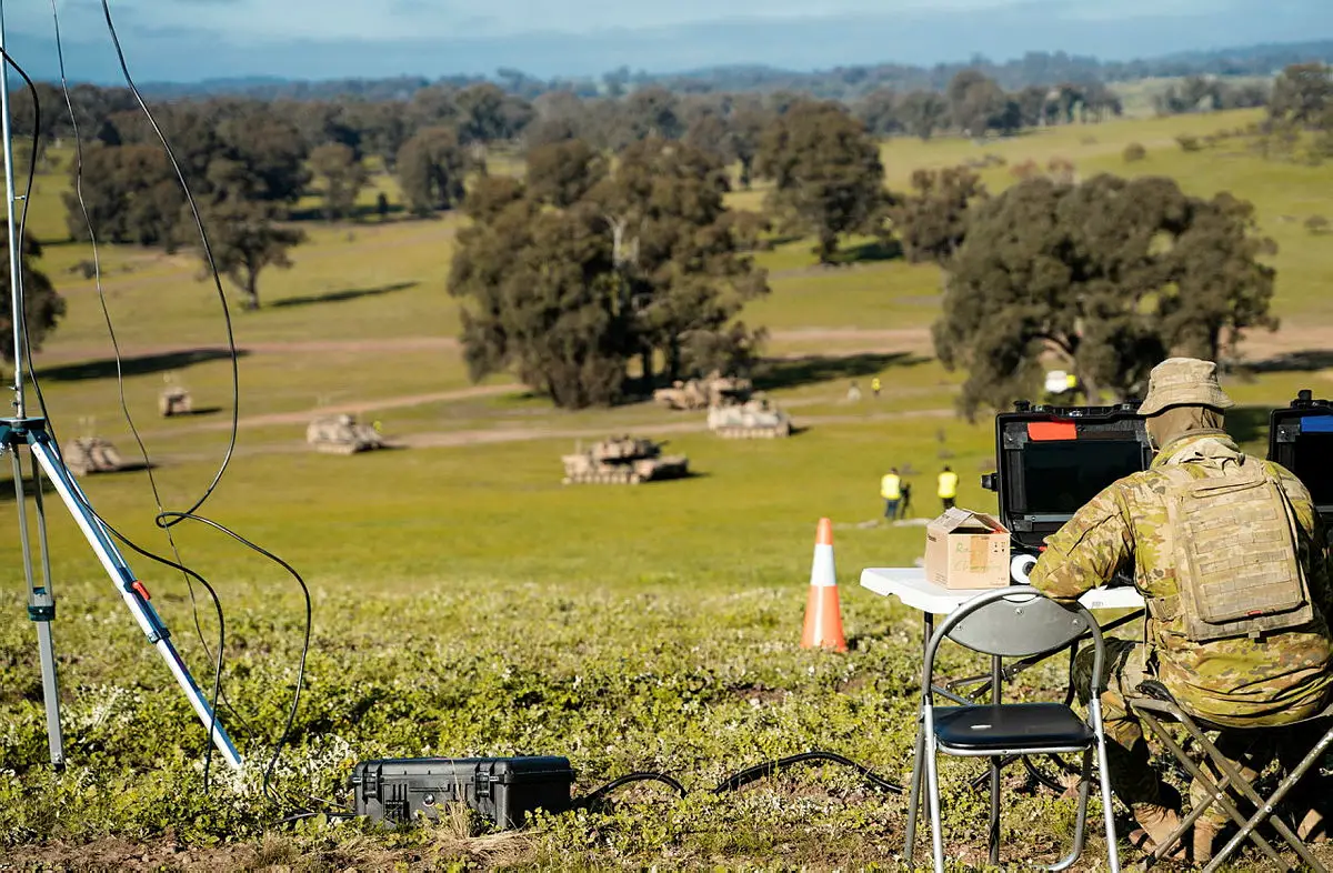 An Australian soldier monitors an autonomous Australian Army M113AS4 Armoured Personal Carrier enhanced as an Optionally Crewed Combat Vehicle (OCCV) as it manoeuvres with larger M1A1 Abrams tanks during a demonstration at Puckapunyal Army Base.
