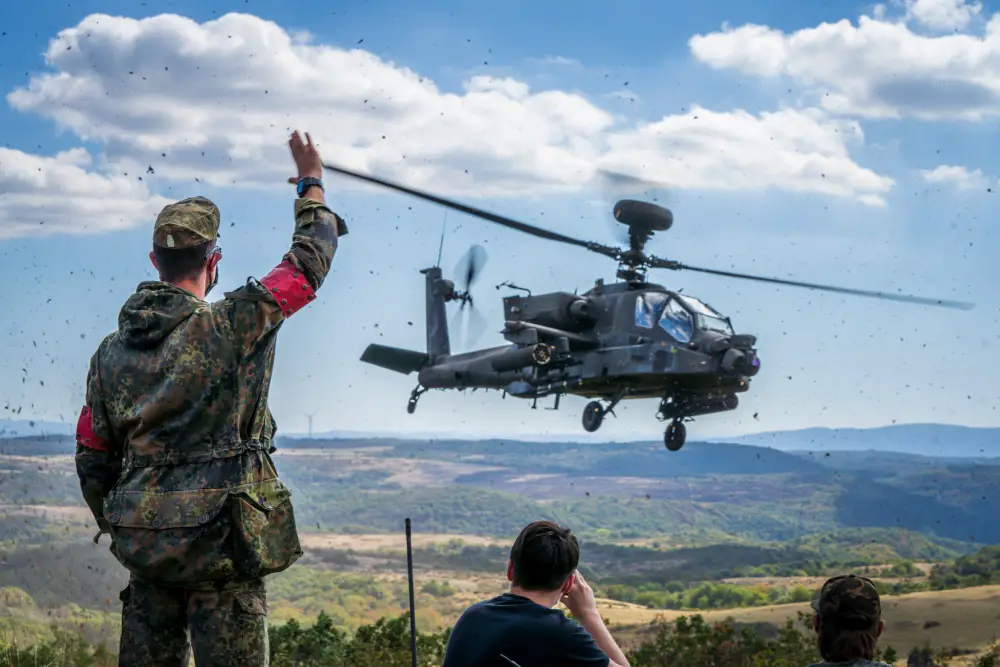 A Bundeswehr Soldier waves to an AH-64 Apache Longbow from A Co, 1-3 Attack Reconnaissance Battalion at Baumholder training area on Sep. 9.