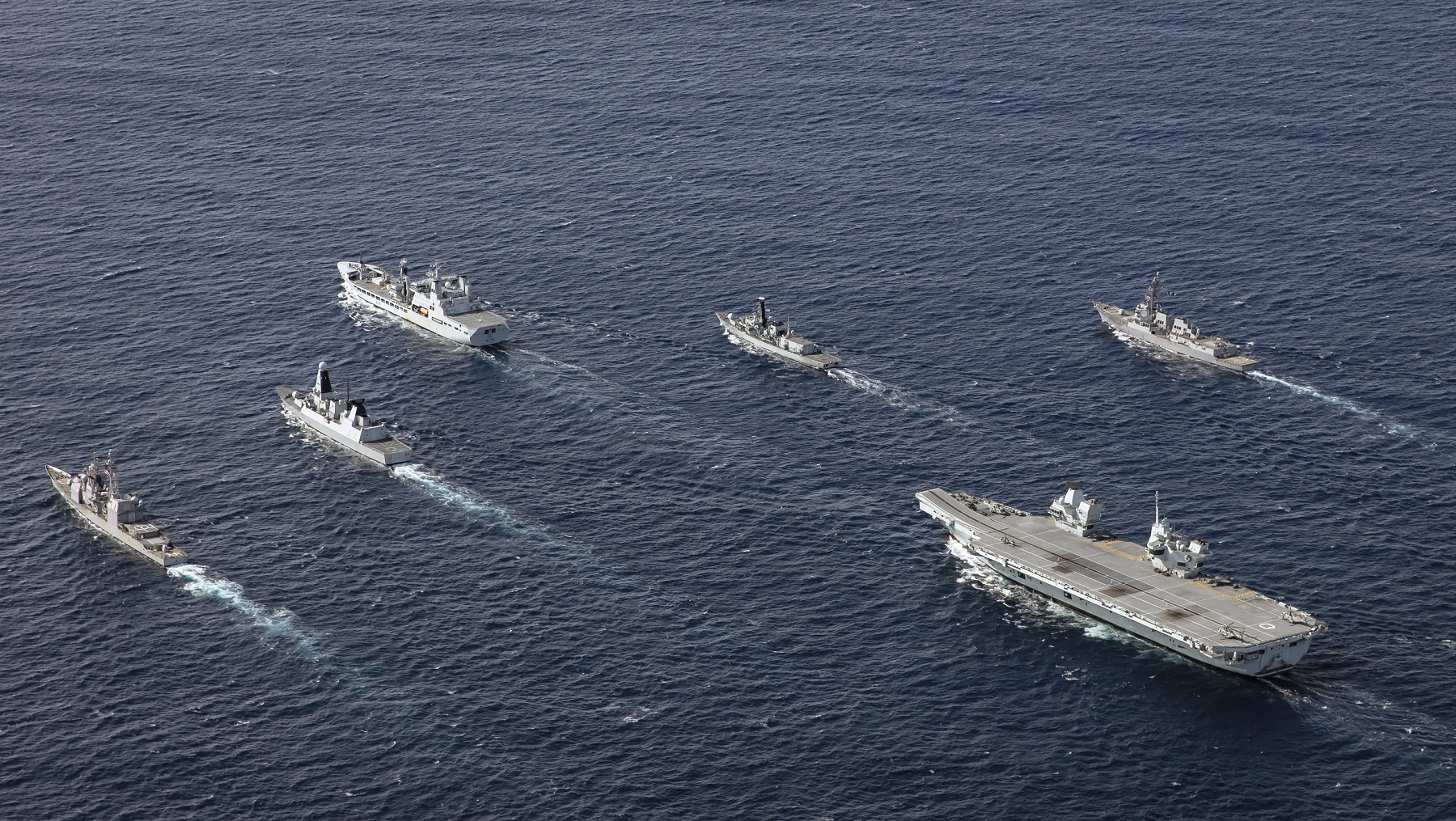 HMS Queen Elizabeth in formation with her Carrier Strike Group. The Carrier Strike Group comprises RFA Tideforce in the lead with HMS Northumberland (her right), USS Truxtun (her far right), HMS Dragon (her left), USS Philippine Sea (her far left) with HMS Queen Elizabeth at the rear.