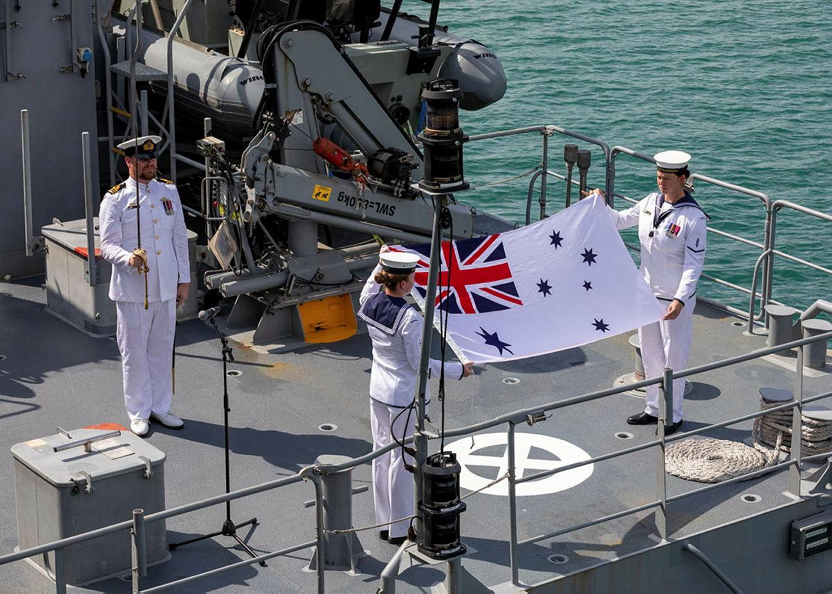 Commanding Officer, HMAS Glenelg Lieutenant Commander Alexander Finnis RAN stands at attention as Leading Seaman Communication Information Systems Kiani Hughes (left) and Able Seaman Maritime Logistics Chef Eliza McGuigan strike the Australian White Ensign for the final time during the decommissioning ceremony held at HMAS Coonawarra, Darwin in the Northern Territory. 