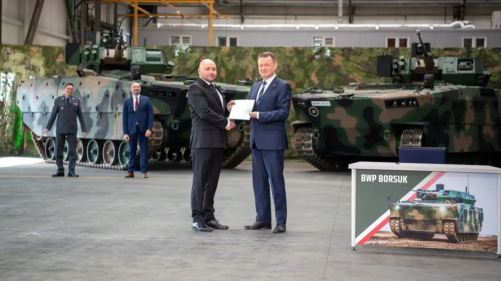 Polish defense minister and HSW chief executive stand in front of Borsuk infantry combat vehicles.