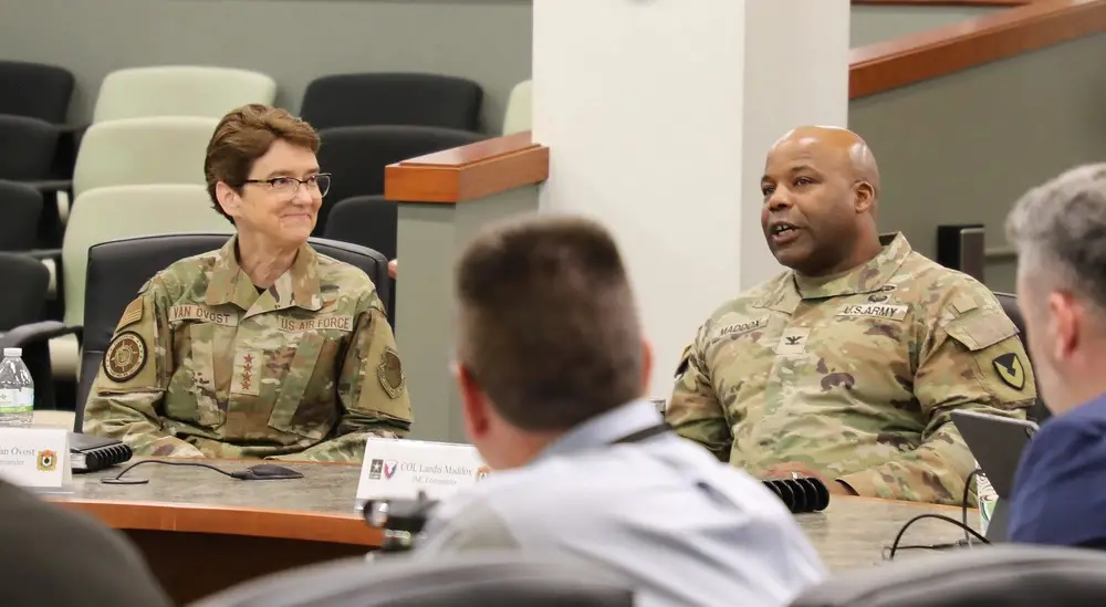 Gen. Jacqueline Van Ovost (left), the commander of U.S. Transportation Command, listens to Col. Landis Maddox (right), the commander of Joint Munitions Command, speak on April 10 at JMC’s headquarters in Rock Island, Illinois.