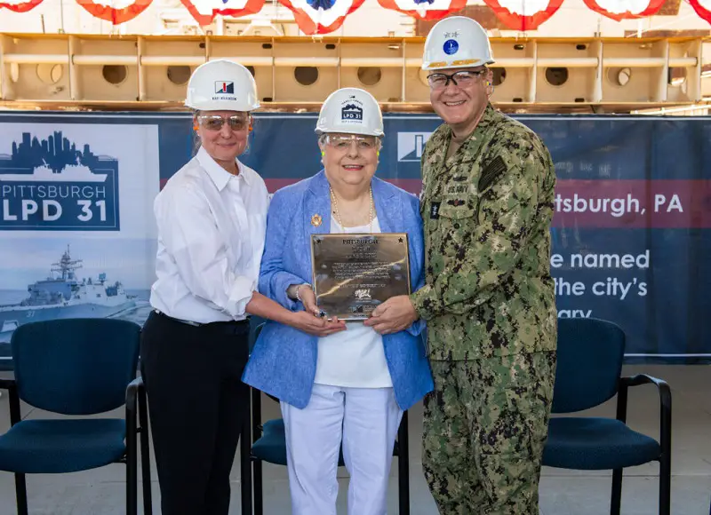 Ship Sponsor Nancy Urban holds the steel plate that will be welded inside LPD 31. Pictured with Urban are (left to right) Ingalls Shipbuilding President Kari Wilkinson and Rear Admiral Tom Anderson, United States Navy, Program Executive Officer for Ships. 
