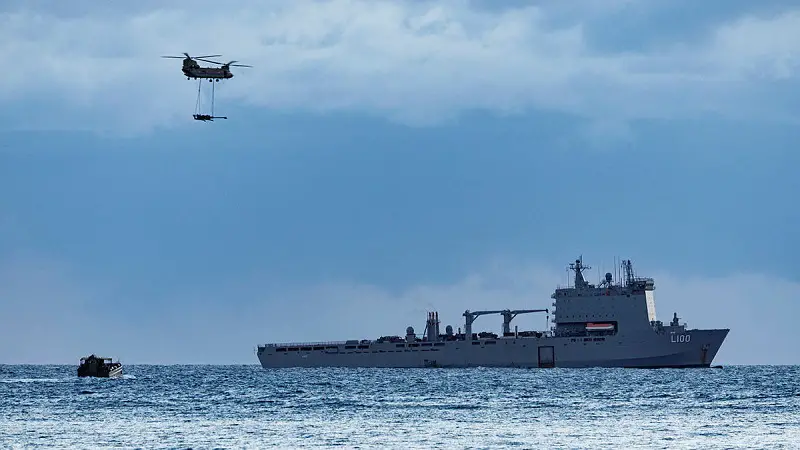 An Australian Army CH-47 Chinook with an underslung M777 howitzer fly over HMAS Choules during the reconstitution of the Australian Amphibious Force during Exercise Sea Raider 2023.
