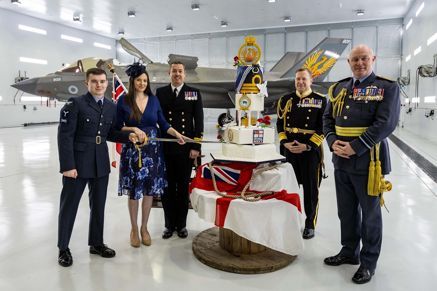 A cake produced especially for the 809 Naval Air Squadron Recommissioning Ceremony is cut by the newest member of the Squadron and the wife of Commander Nick Smith, as Commander Smith, Vice Admiral Martin Connell and Air Marshal Harvey Smith watch on.