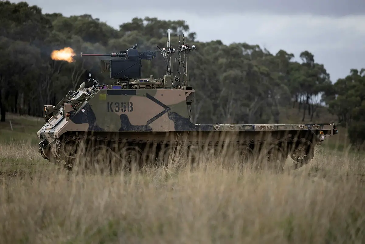 An Australian Army M113AS4 armoured logistics vehicle, fitted with optionally crewed combat vehicle technology and a remote weapon station, fires from a support-by-fire position during a human-machine team exercise at Puckapunyal Military Area.