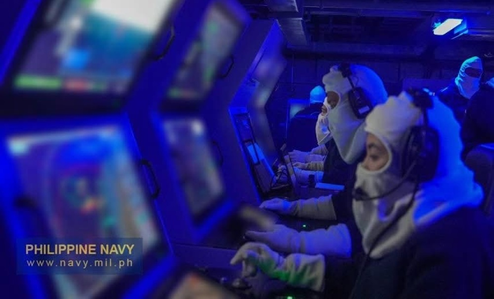 The sailor is seated at a tactical console and is fully enveloped in white anti-flash gear, including a mask covering their lower face and white gloves, with only their eyes and hands exposed.